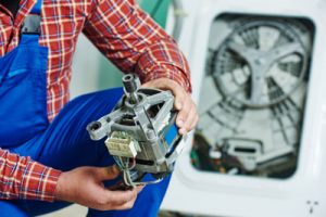 Washing machine repair. Repairer hands with electric engine motor in front of damaged unit